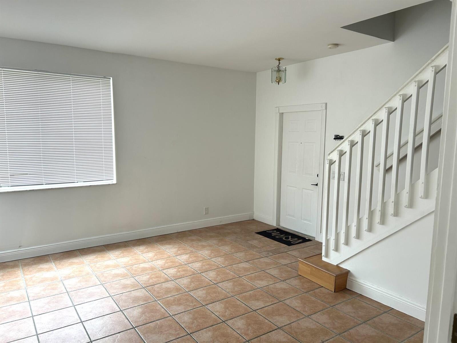 An empty room features tan tile flooring, a white staircase, and a front entry door — 4361 Dogwood Circle, Weston FL 33331, WESTON, FL