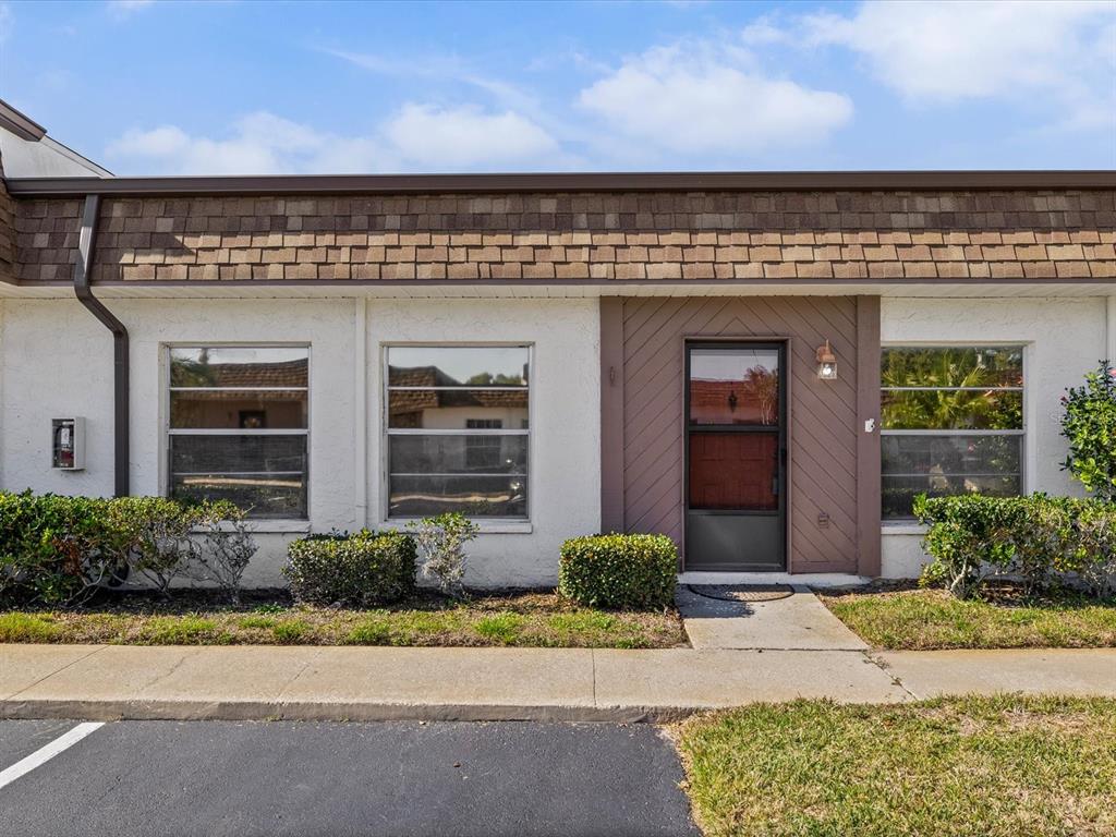 The exterior of a single-story building features white stucco walls, brown trim, and a shingled roof — 6037 CHESHAM DRIVE UNIT 7, NEW PORT RICHEY, FL