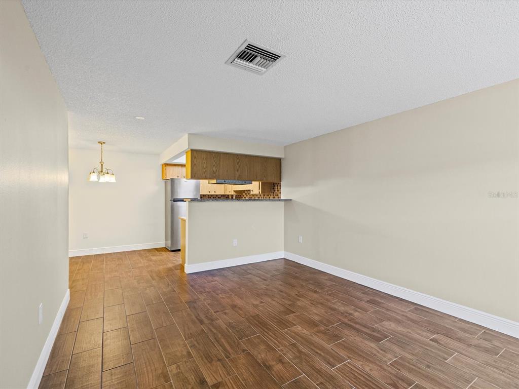 An open-concept living and dining area features wood-look tile flooring and a kitchen breakfast bar — 6037 CHESHAM DRIVE UNIT 7, NEW PORT RICHEY, FL
