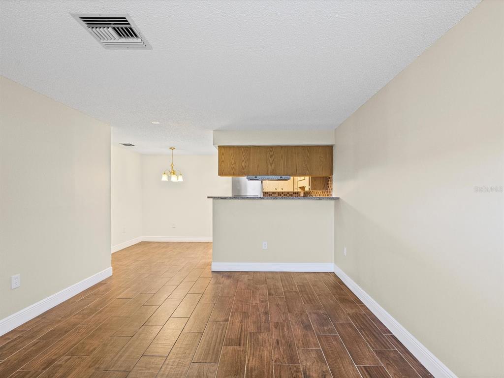 A living area with wood-look tile flooring leads to a kitchen with a breakfast bar — 6037 CHESHAM DRIVE UNIT 7, NEW PORT RICHEY, FL
