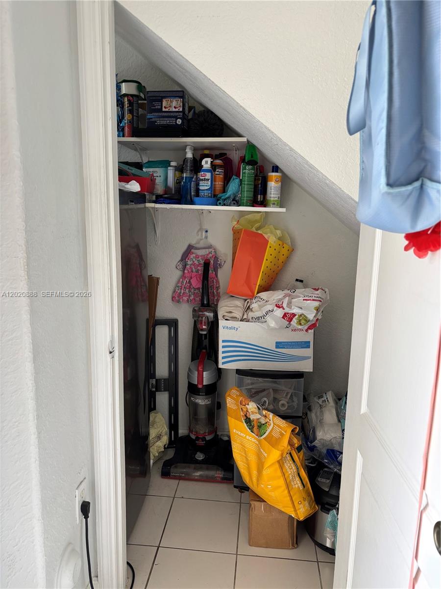 A small under-stair storage closet contains shelves with cleaning supplies, a vacuum, and various boxes — 6920 NW 177th St # Q101, Hialeah FL 33015, HIALEAH, FL