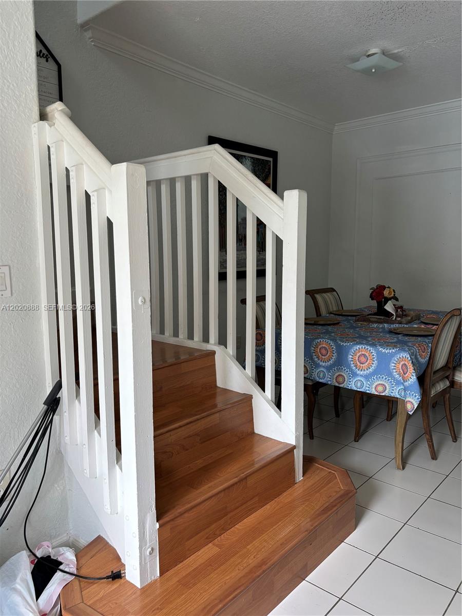 A wooden staircase with white railings sits next to a dining area with tiled floors — 6920 NW 177th St # Q101, Hialeah FL 33015, HIALEAH, FL