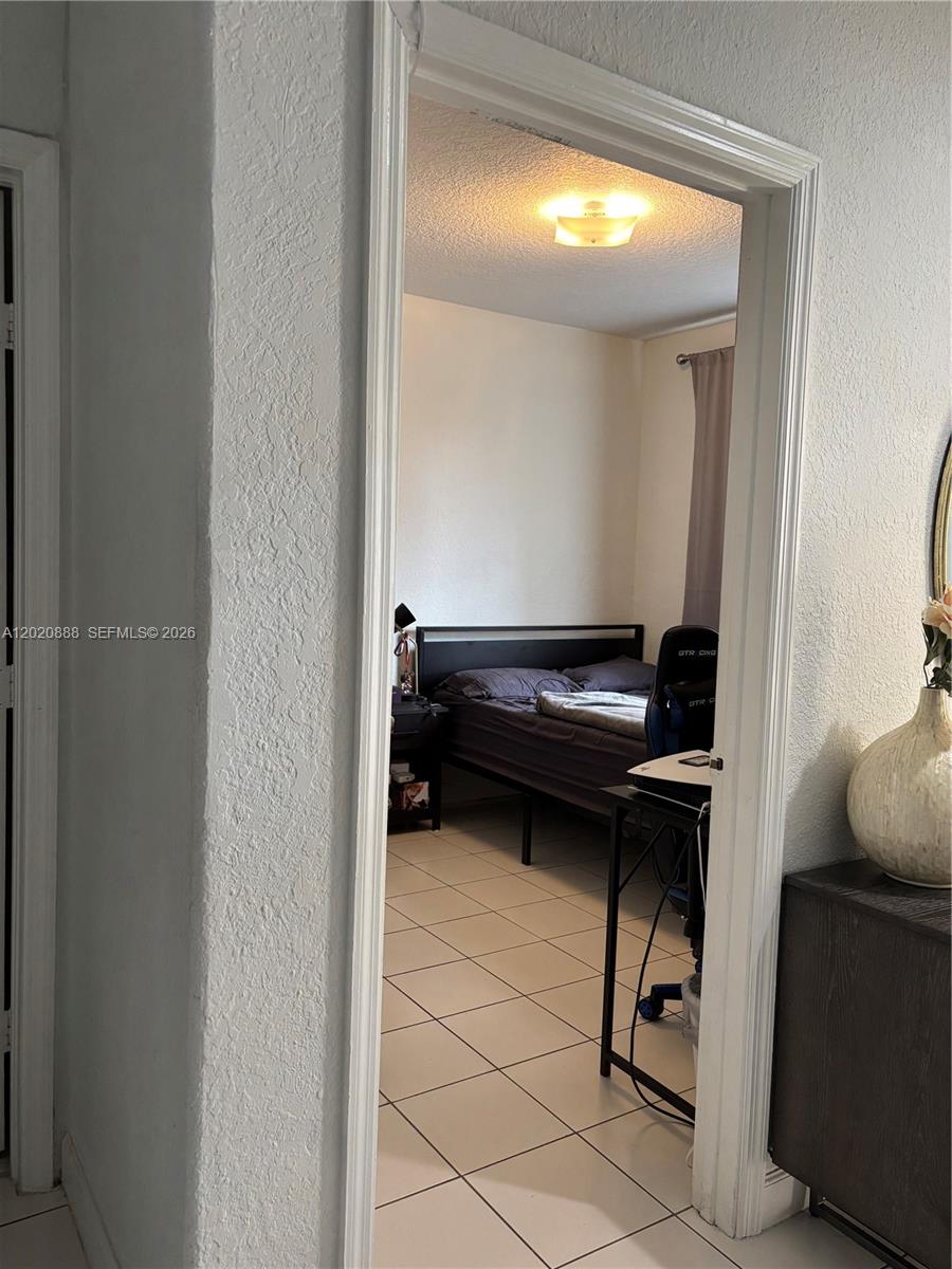 A bedroom with a bed and desk is viewed through a doorway with tiled floors — 6920 NW 177th St # Q101, Hialeah FL 33015, HIALEAH, FL
