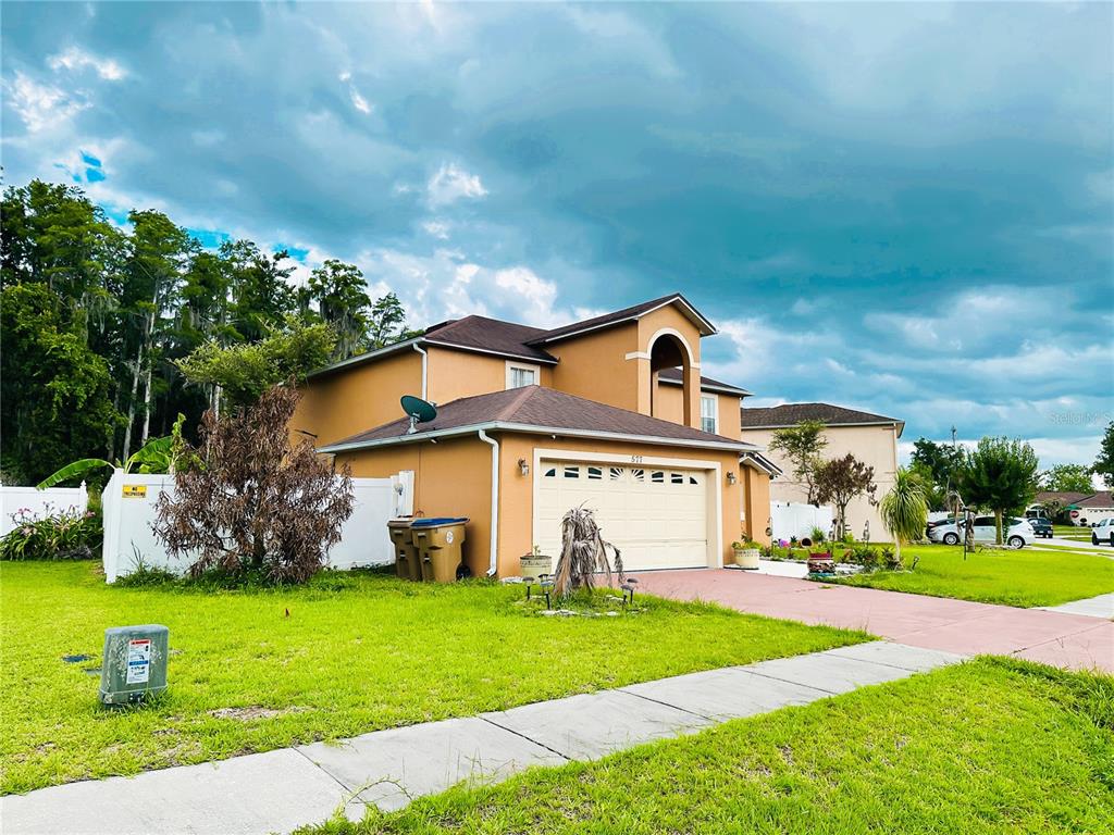 A two-story, tan-colored suburban house with a two-car garage and a paved driveway — 577 PINEHURST COVE, KISSIMMEE, FL