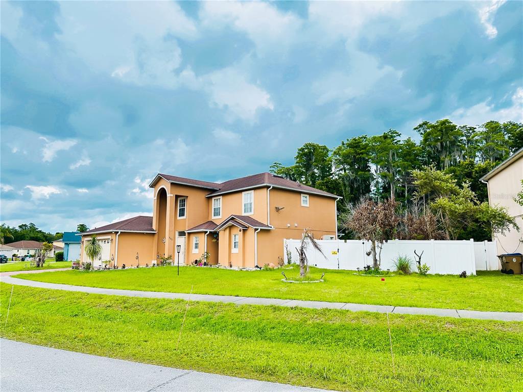 A two-story tan house with a brown roof stands on a grassy corner lot — 577 PINEHURST COVE, KISSIMMEE, FL