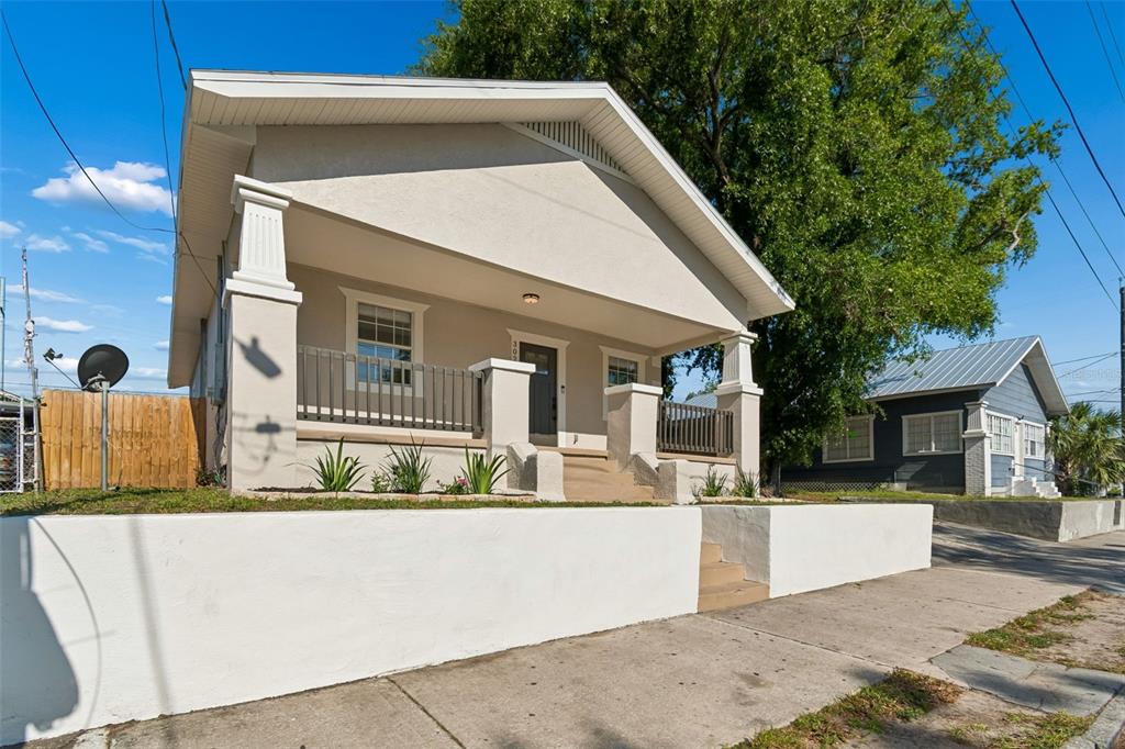 A single-story house with a front porch, white stucco walls, and a concrete retaining wall — 3022 SANCHEZ STREET, TAMPA, FL
