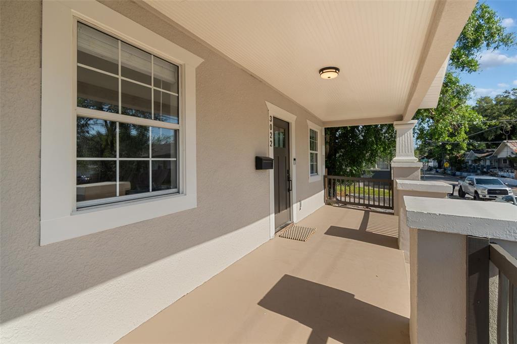 A covered front porch with a dark door, a window, and a wooden railing — 3022 SANCHEZ STREET, TAMPA, FL