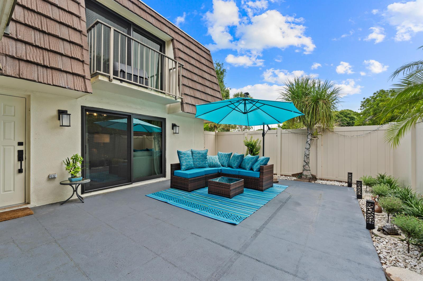 A patio features a sectional sofa, a blue umbrella, and a rug against a house — 7707 77th Way # 7707, West Palm Beach FL 33407, WEST PALM BEACH, FL