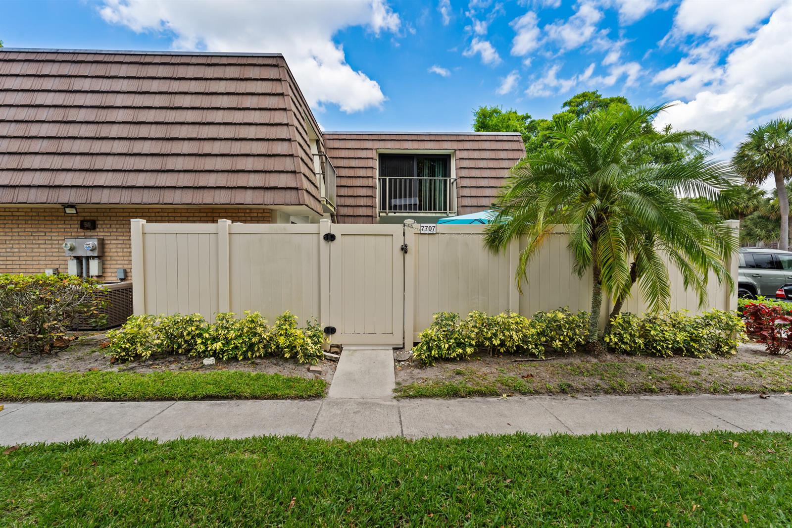 A tan vinyl fence with a central gate stands in front of a two-story building — 7707 77th Way # 7707, West Palm Beach FL 33407, WEST PALM BEACH, FL