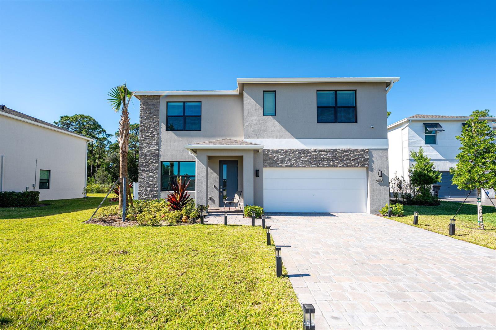 A two-story house with a stone facade, a white garage door, and a paved driveway — 6016 SE Violet Lane, Stuart FL 34997, STUART, FL