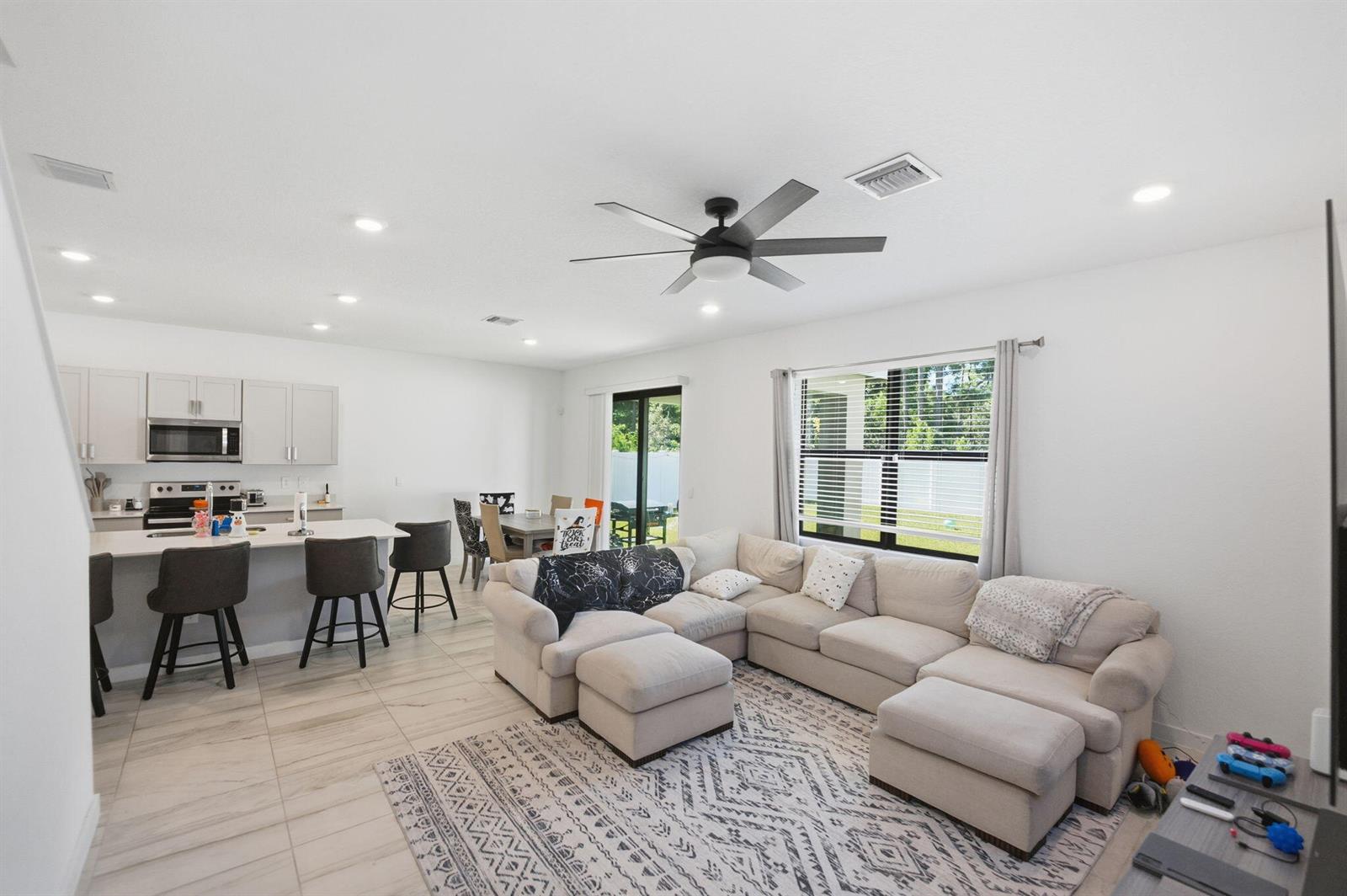 An open-concept living room and kitchen featuring a sectional sofa, island seating, and tile flooring — 6016 SE Violet Lane, Stuart FL 34997, STUART, FL