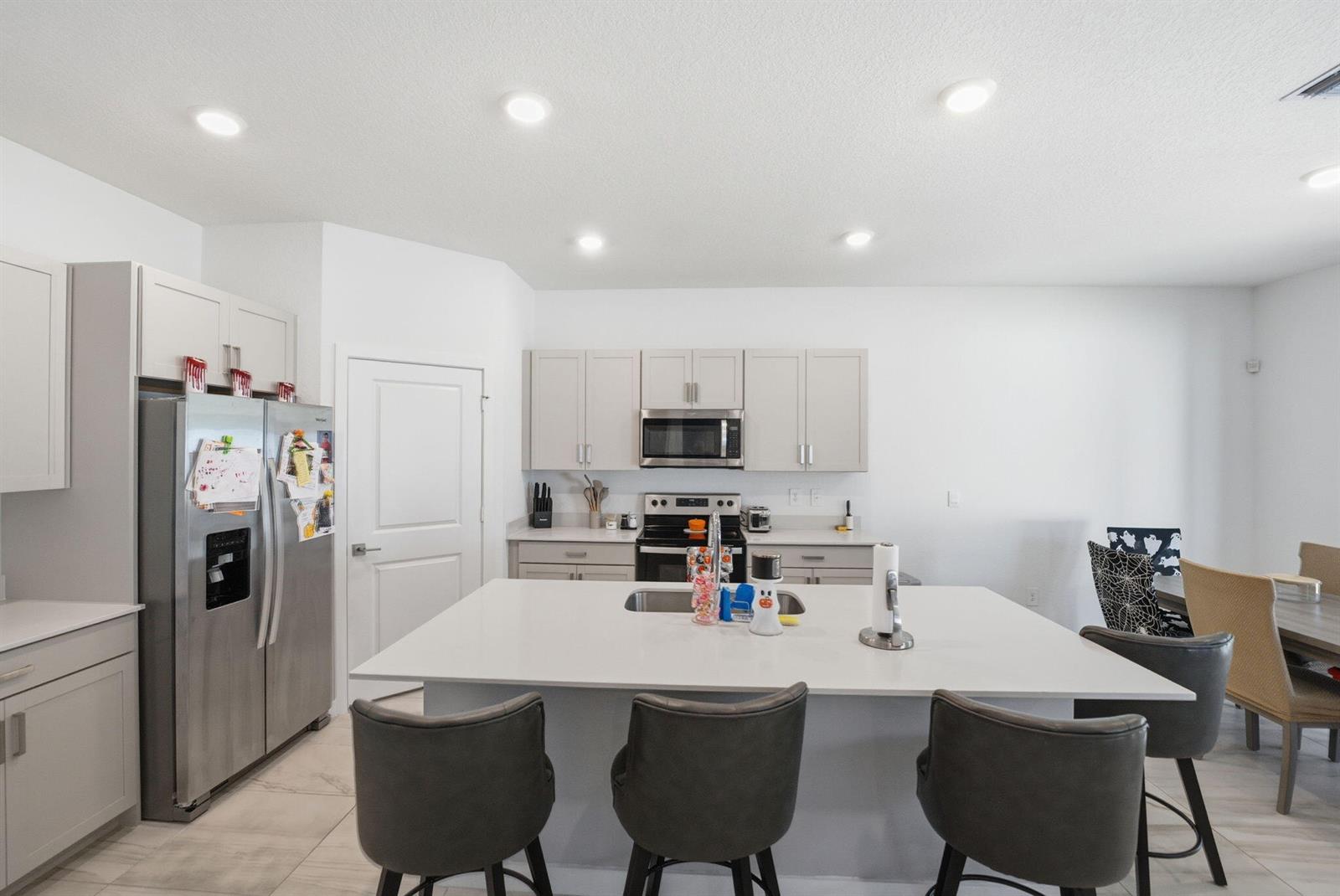 A modern kitchen features light gray cabinets, stainless steel appliances, and a large central island — 6016 SE Violet Lane, Stuart FL 34997, STUART, FL