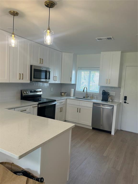 A modern kitchen features white cabinetry, stainless steel appliances, quartz countertops, and light wood flooring — 1624 STICKNEY POINT ROAD UNIT 101, SARASOTA, FL