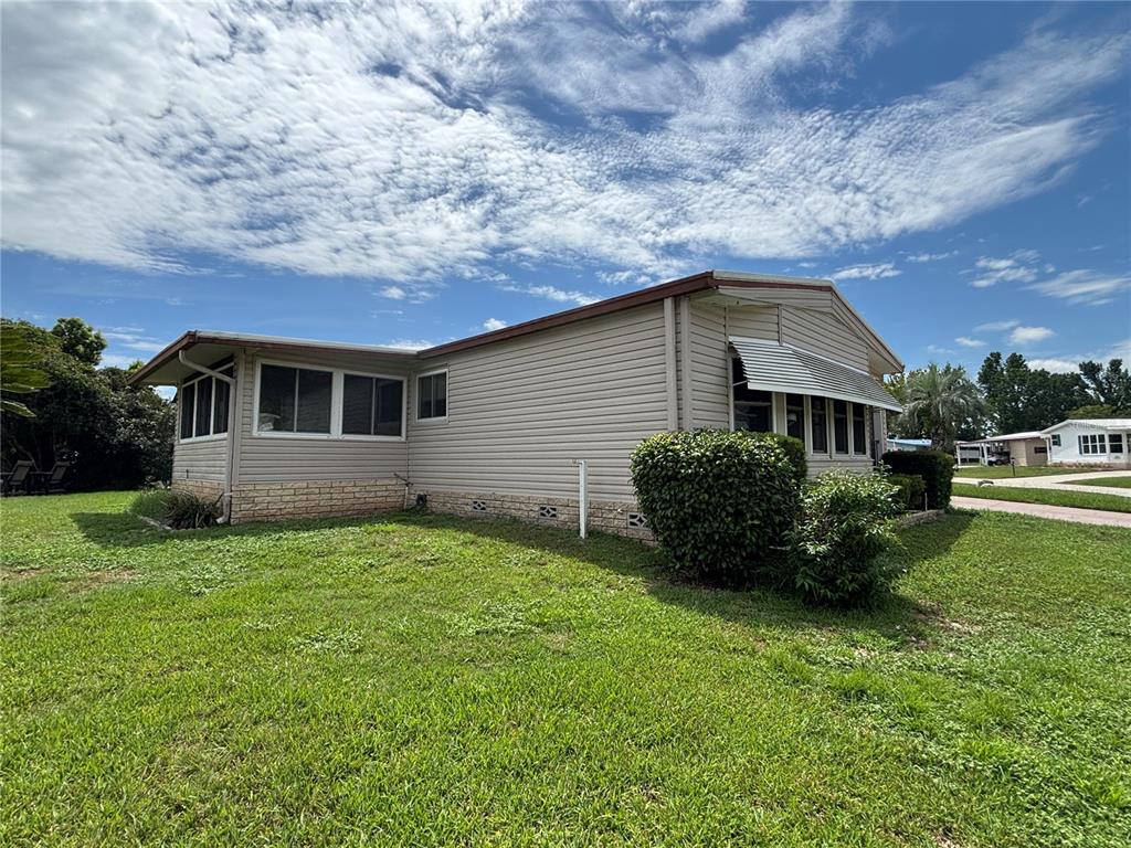 A beige mobile home with a screened-in porch sits on a grassy lot — 2541 AMYRIS COURT UNIT 611, ZELLWOOD, FL