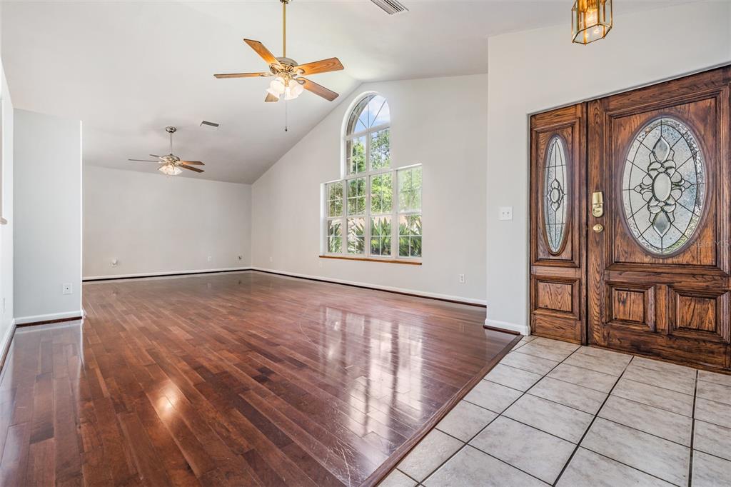 A living room with hardwood floors, vaulted ceilings, two ceiling fans, and a large arched window — 6536 NORTHLAKE DRIVE, ZEPHYRHILLS, FL