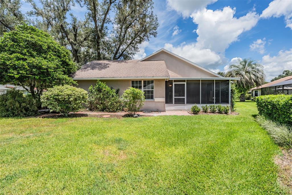 The exterior view shows the back of a house with a screened-in patio and lawn — 6536 NORTHLAKE DRIVE, ZEPHYRHILLS, FL