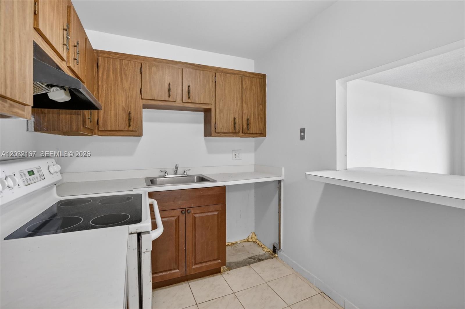 A kitchen with wood cabinets and tile floors opens to a living area with balcony — 4174 Inverrary Dr # 805, Lauderhill FL 33319, LAUDERHILL, FL