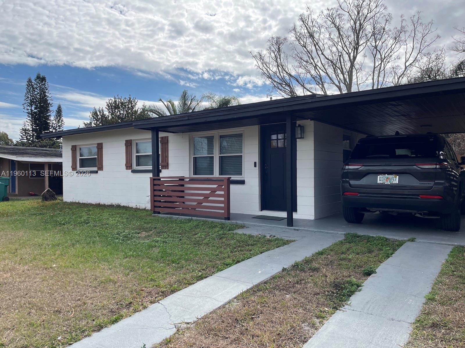 A white single-story house with a carport, dark trim, and a small wooden front fence — 2253 Dordon Drive, Melbourne FL 32935, MELBOURNE, FL