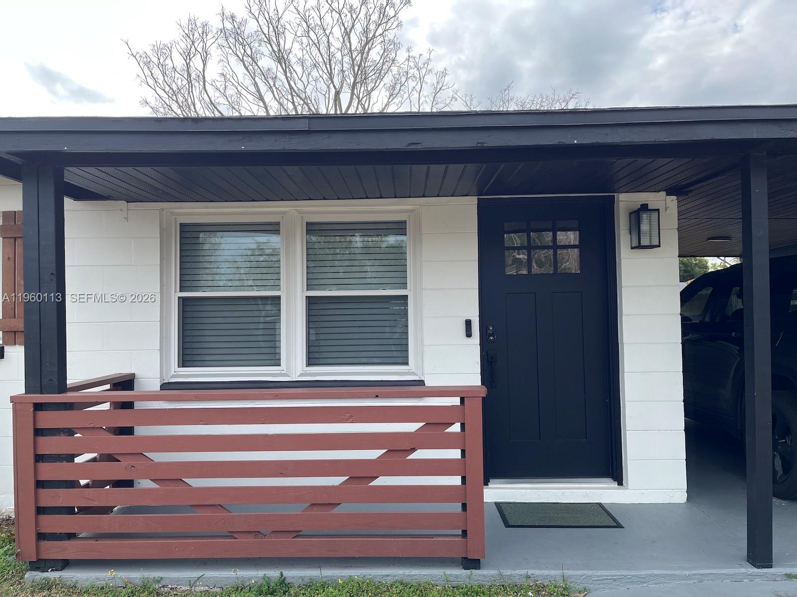A white house exterior features a black front door, a window, and a wooden railing — 2253 Dordon Drive, Melbourne FL 32935, MELBOURNE, FL