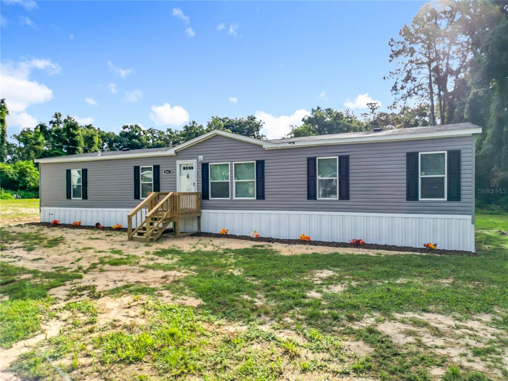 A gray manufactured home with white skirting and a wooden front porch sits on grass — 8561 NW 13TH COURT, OCALA, FL