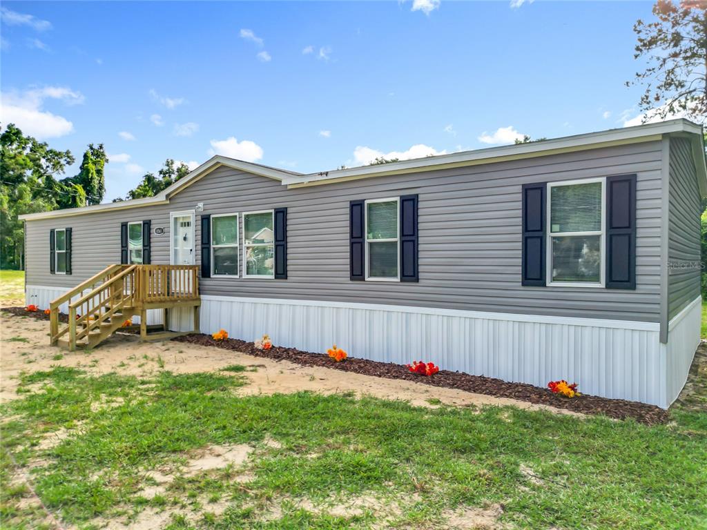 A grey manufactured home with white skirting, dark shutters, and a wooden front porch — 8561 NW 13TH COURT, OCALA, FL