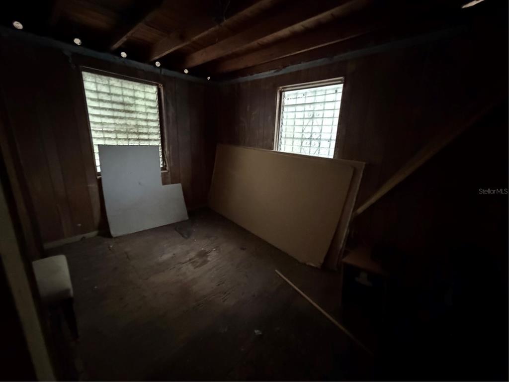 An unfinished room with wood-paneled walls, exposed ceiling joists, and two glass block windows — 3612 N 23RD STREET, TAMPA, FL