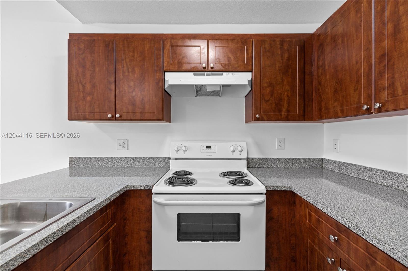 A kitchen features dark wood cabinets, granite countertops, and a white electric stove — 2421 W 78th St # 104, Hialeah FL 33016, HIALEAH, FL