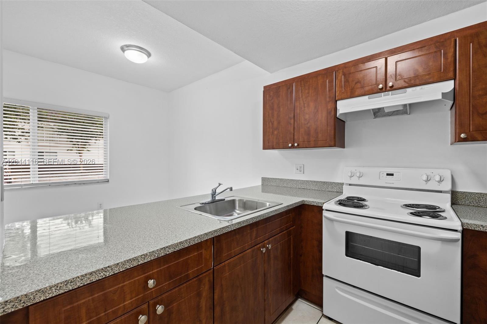 A kitchen features dark wood cabinets, granite countertops, and a white electric stove — 2421 W 78th St # 104, Hialeah FL 33016, HIALEAH, FL