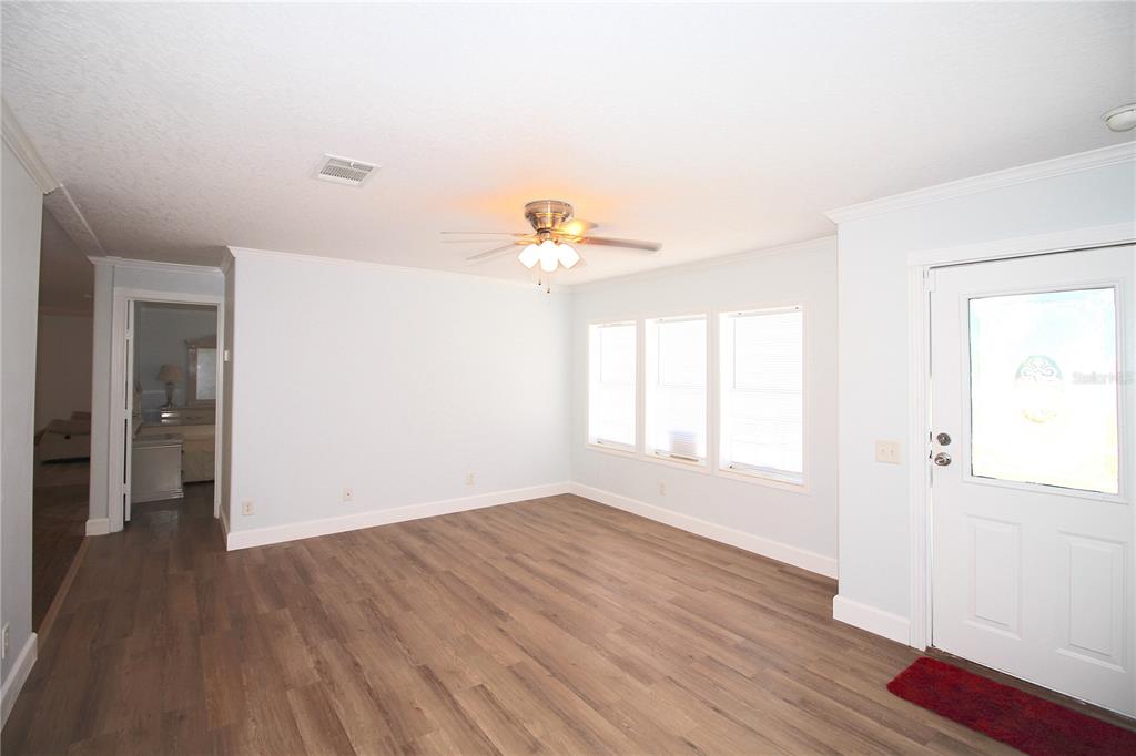 A living room with light blue walls, wood-look flooring, a ceiling fan, and a door — 9222 E RIVERBLUFF COURT, INVERNESS, FL