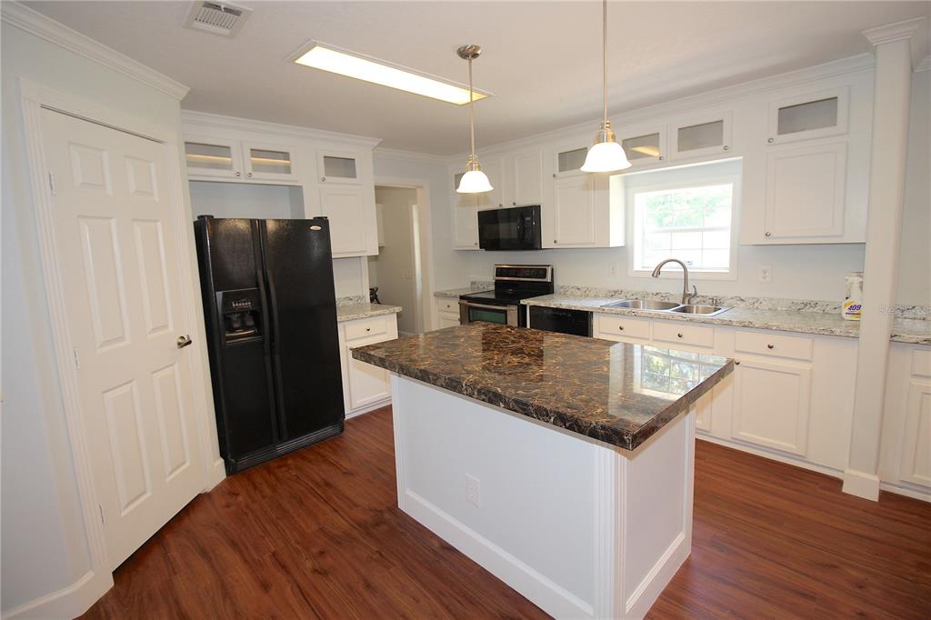 A kitchen features white cabinets, a dark granite island, black appliances, and wood-look flooring — 9222 E RIVERBLUFF COURT, INVERNESS, FL