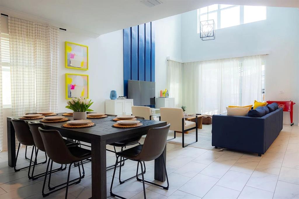 A dining area with a dark table opens into a living room with high ceilings — 4294 PARAGRAPH DRIVE, KISSIMMEE, FL