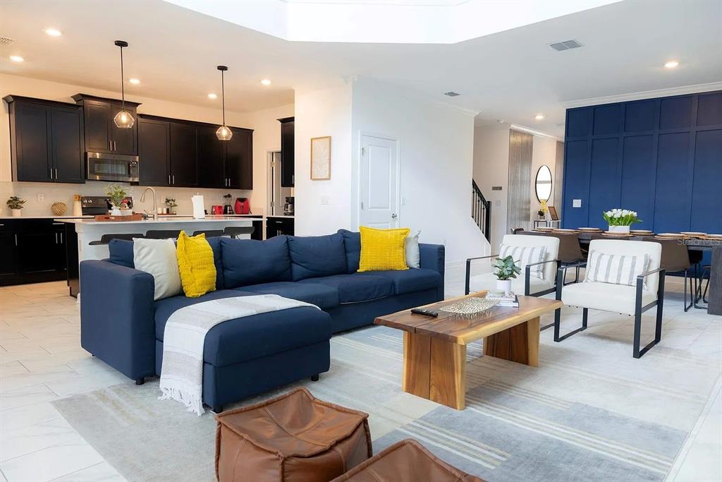 An open-concept living room features a blue sectional sofa, a wooden coffee table, and kitchen — 4294 PARAGRAPH DRIVE, KISSIMMEE, FL