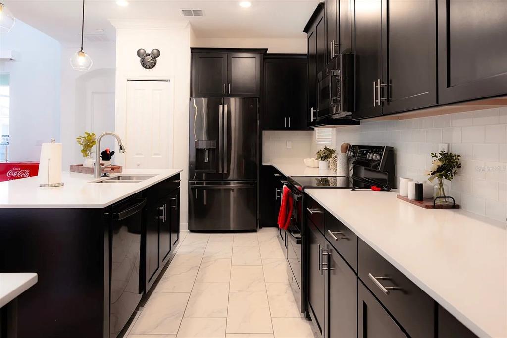 A modern kitchen features black cabinetry, white countertops, stainless steel appliances, and light tile flooring — 4294 PARAGRAPH DRIVE, KISSIMMEE, FL