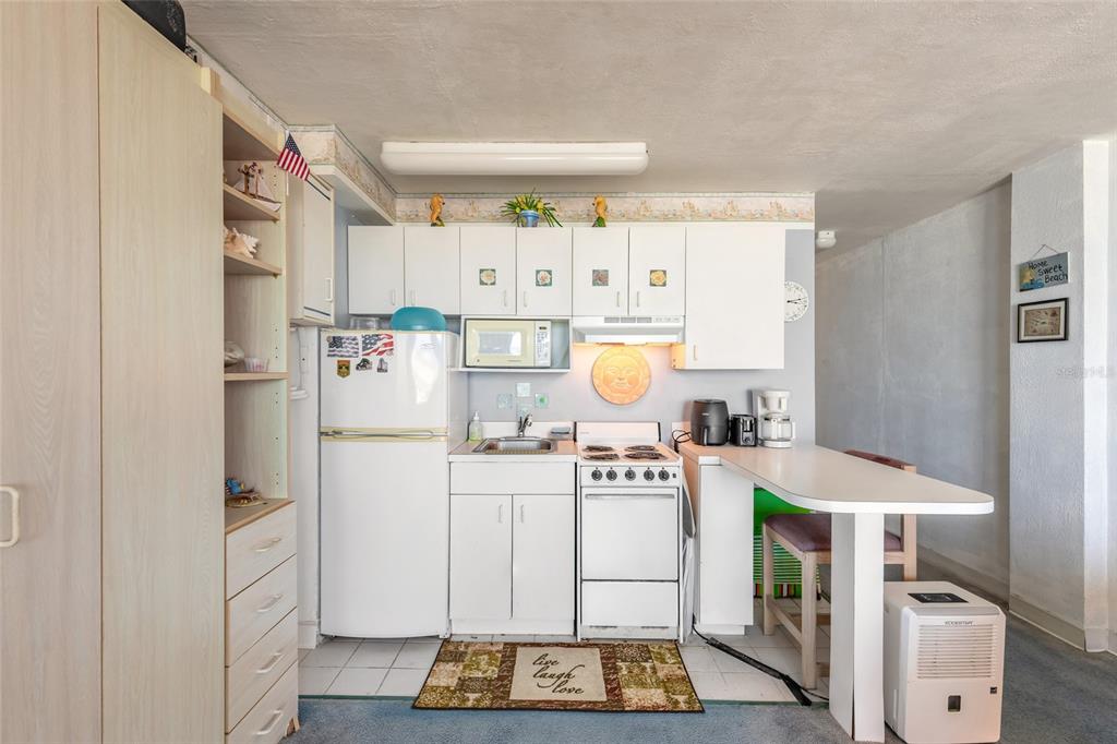 A small kitchen features white cabinets, a white refrigerator, a stove, and a breakfast bar — 701 S ATLANTIC AVENUE UNIT 417, DAYTONA BEACH, FL