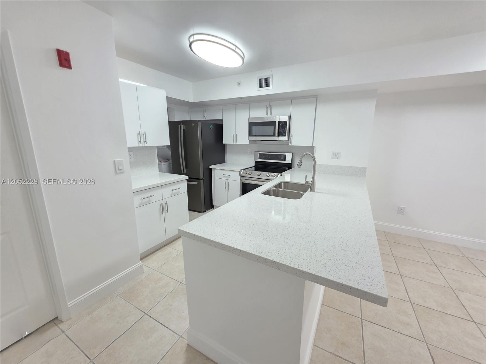 A white kitchen features a quartz island, stainless steel appliances, and light-colored tile flooring — 2620 S University Dr # 111, Davie FL 33328, DAVIE, FL