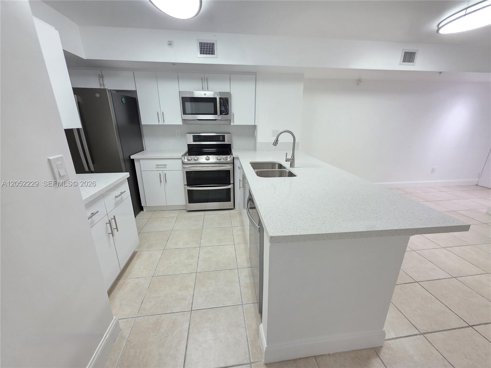 A modern kitchen features white cabinets, stainless steel appliances, and a large quartz-topped island — 2620 S University Dr # 111, Davie FL 33328, DAVIE, FL
