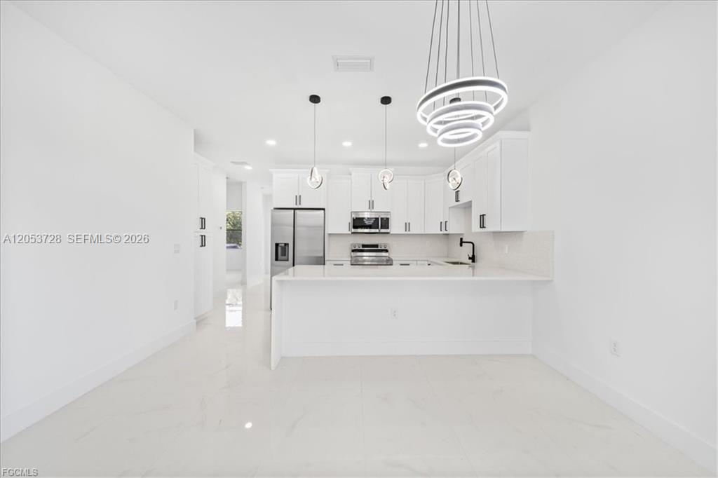 A modern white kitchen features a peninsula, stainless steel appliances, and minimalist pendant lighting — 849 E Wolverine, Lehigh Acres FL 33974, LEHIGH ACRES, FL