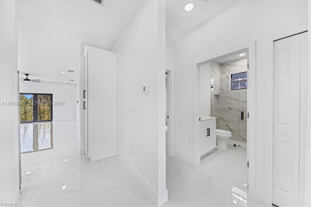 A white hallway leads to a bathroom with marble-style tile and a glass shower — 849 E Wolverine, Lehigh Acres FL 33974, LEHIGH ACRES, FL