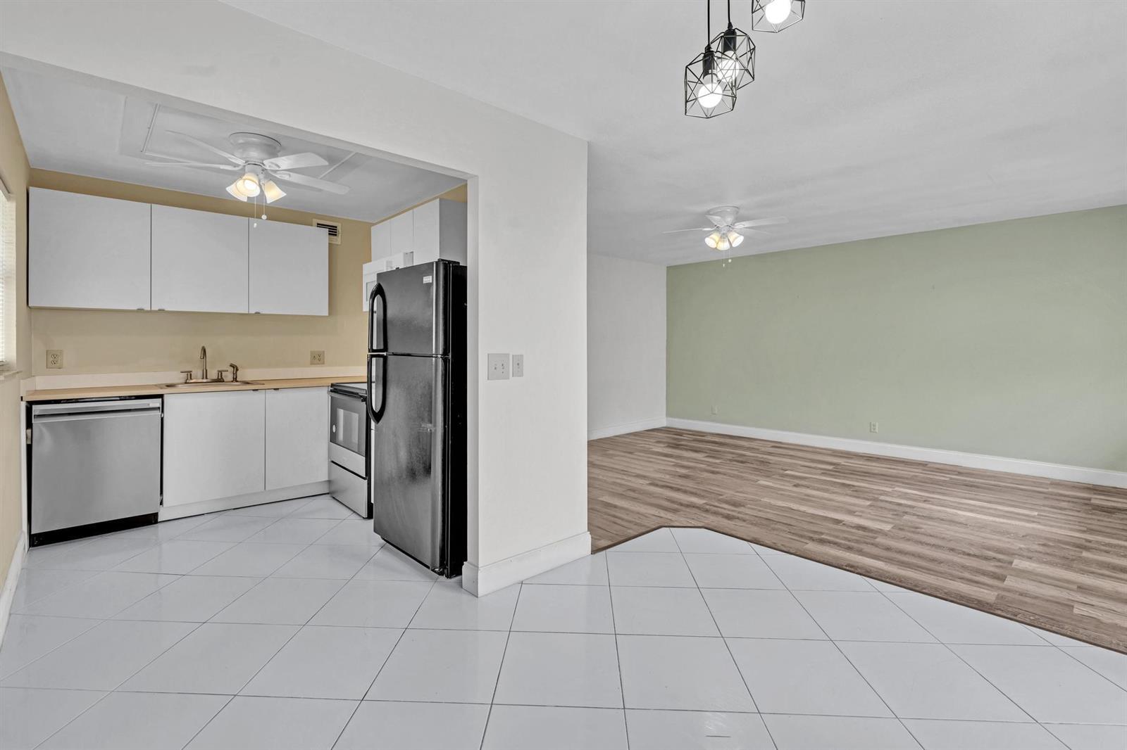 A kitchen with white cabinets and tile flooring opens into a living area with wood-look flooring — 365 Flanders # H, Delray Beach FL 33484, DELRAY BEACH, FL