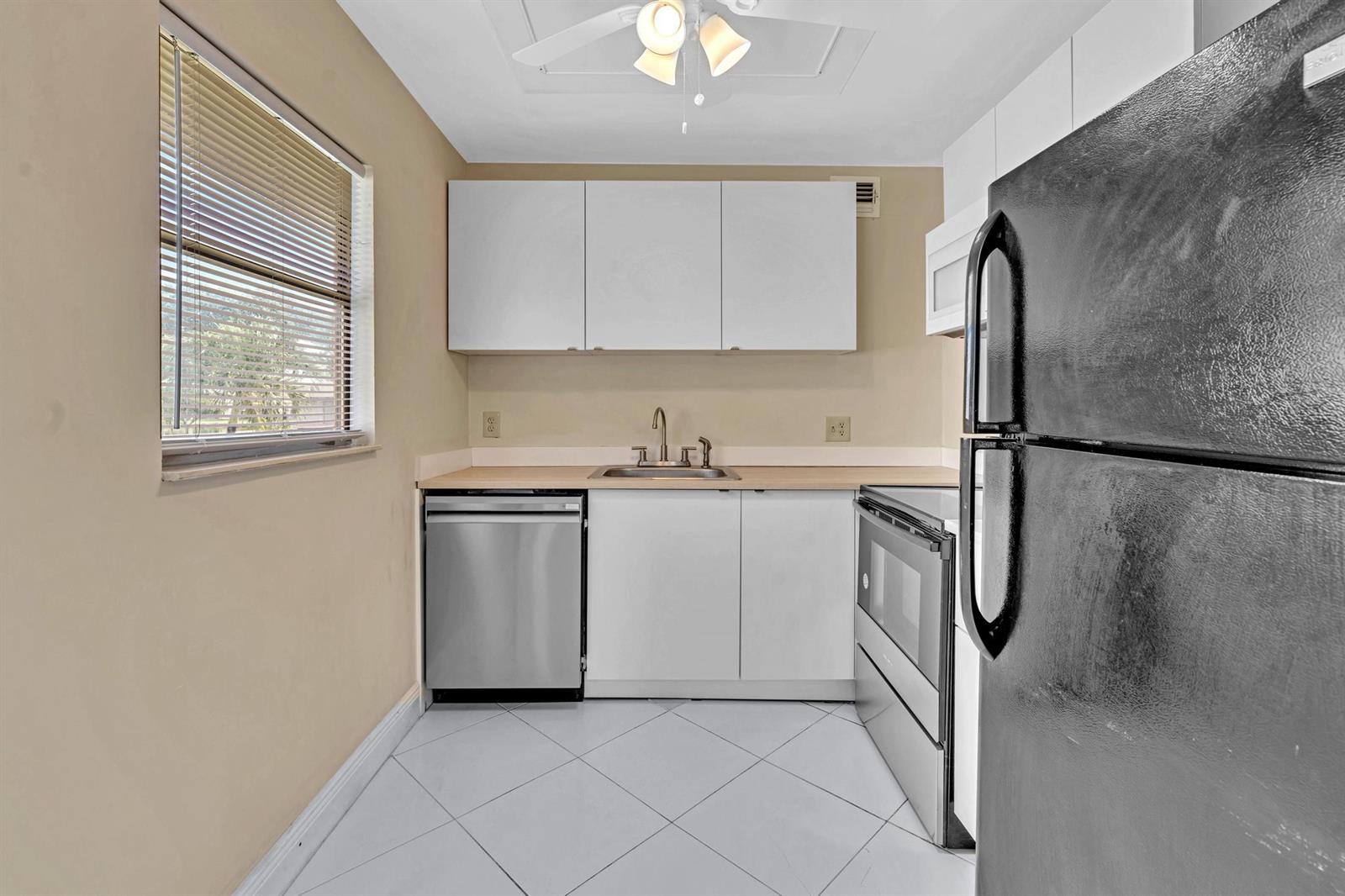 A small kitchen features white cabinets, stainless steel appliances, a window, and tiled flooring — 365 Flanders # H, Delray Beach FL 33484, DELRAY BEACH, FL