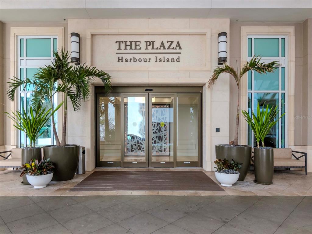 The exterior entrance of a building features sliding glass doors, potted palm trees, and signage — 450 KNIGHTS RUN AVENUE UNIT 1501, TAMPA, FL