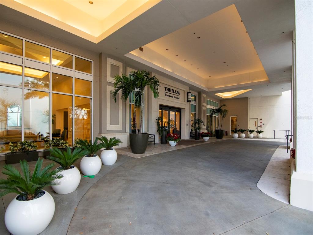 The exterior entrance of a building features a covered driveway, glass doors, and potted plants — 450 KNIGHTS RUN AVENUE UNIT 1501, TAMPA, FL