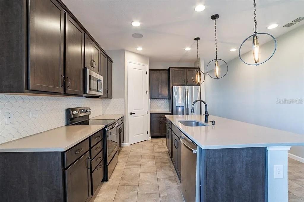 A kitchen with dark cabinets, a large island, stainless steel appliances, and light-colored countertops — 203 SANGMON COURT, GROVELAND, FL