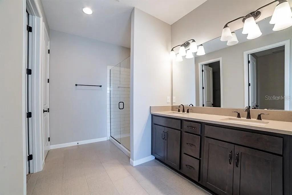 A bathroom features a double vanity with dark cabinets, a mirror, and a glass-enclosed shower — 203 SANGMON COURT, GROVELAND, FL