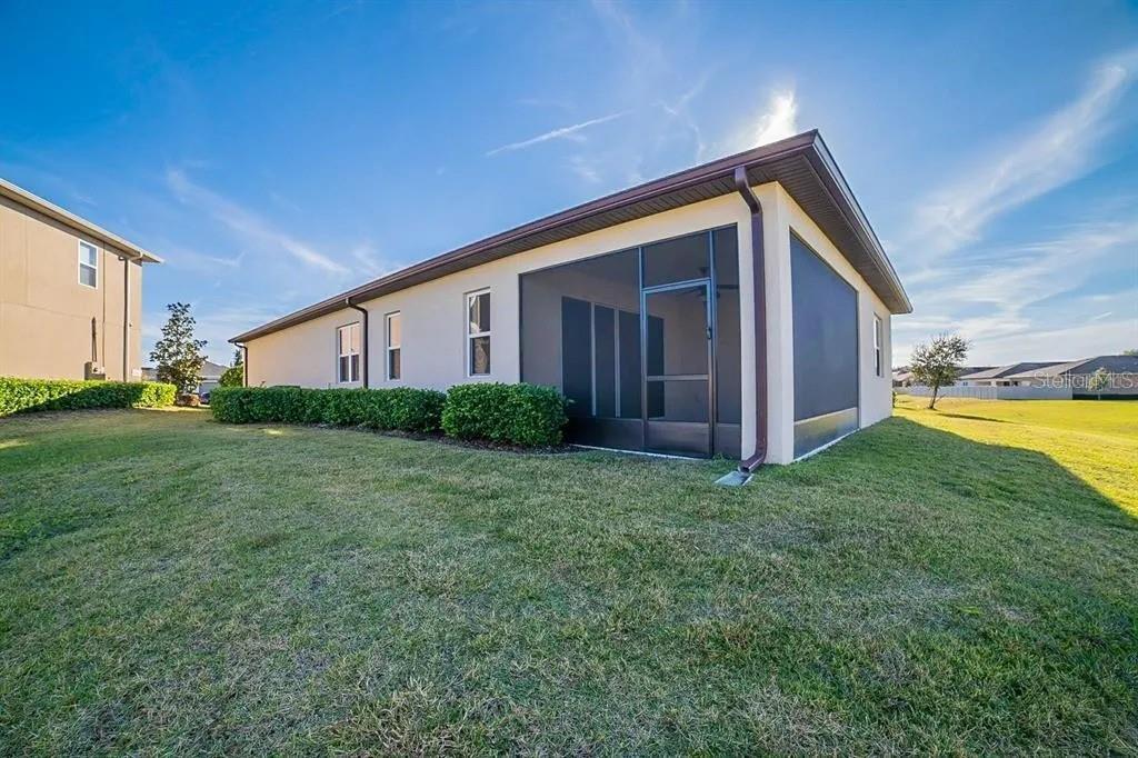 The exterior of a single-story house features a screened-in lanai and a grassy backyard — 203 SANGMON COURT, GROVELAND, FL