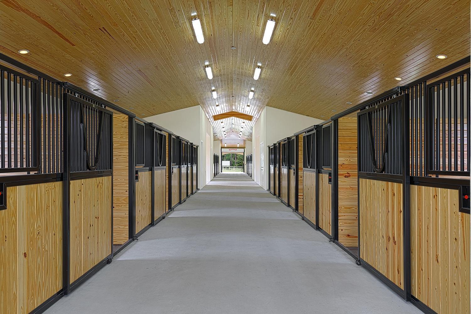 A long, symmetrical horse stable aisle with wood-paneled ceilings, concrete floors, and black metal stalls — 2088 Appaloosa Trail, Wellington FL, WELLINGTON, FL