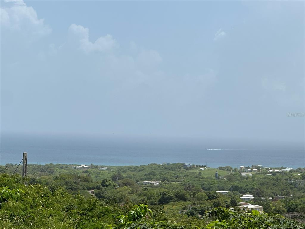A high-angle view shows a lush green landscape overlooking the ocean under a blue sky — COMUNIDAD VILLA BORINQUÉN, VIEQUES, PR