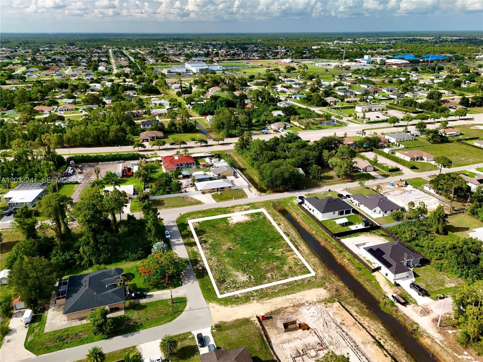 An aerial view shows a vacant rectangular residential lot bordered by a canal and houses — 0 4th St W, Lehigh Acres FL 33971, LEHIGH ACRES, FL