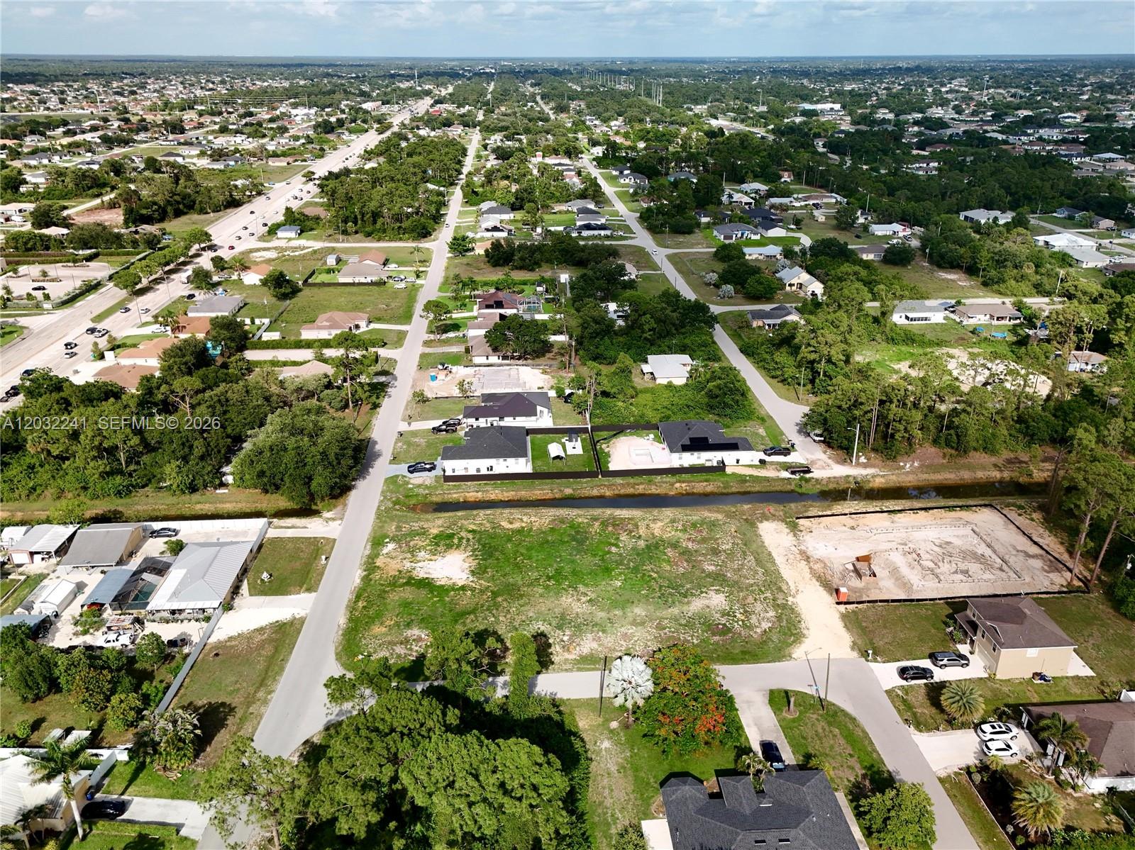 An aerial view shows a residential neighborhood with houses, a canal, and vacant lots — 0 4th St W, Lehigh Acres FL 33971, LEHIGH ACRES, FL