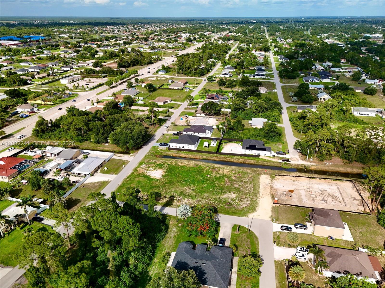 An aerial view shows a suburban neighborhood with houses, undeveloped lots, and a drainage canal — 0 4th St W, Lehigh Acres FL 33971, LEHIGH ACRES, FL